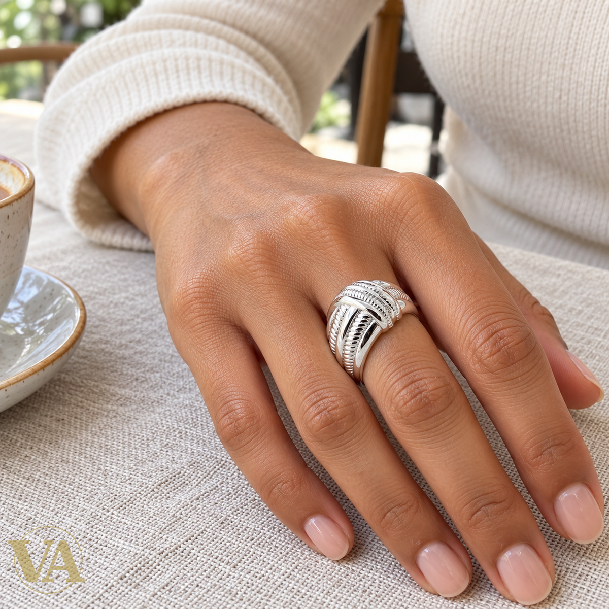 Bague argent rhodié rubans croisés cannelés portée sur une main à table