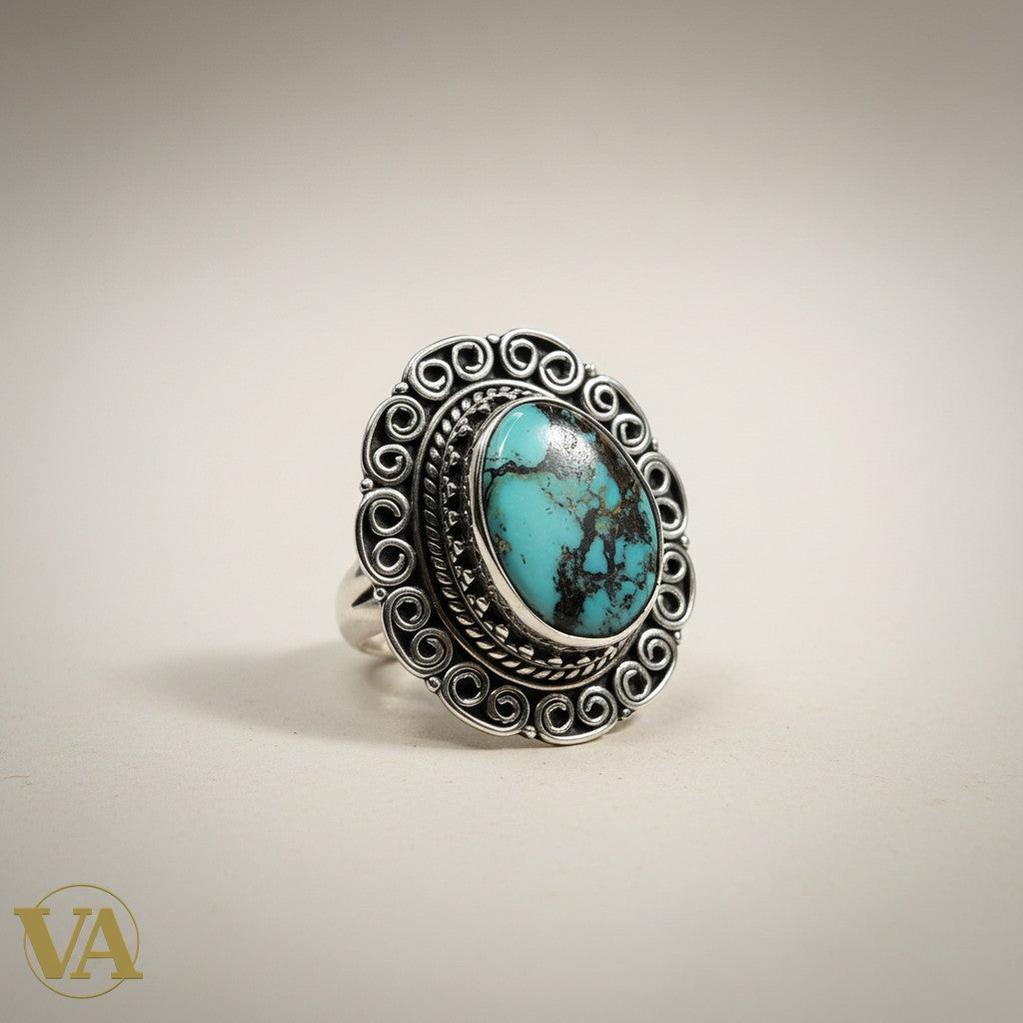 Bague femme Vindicta en argent 925 avec un cabochon turquoise ovale aux veines naturelles, serti travaillé et décor ciselé en volutes. Style bohème chic.