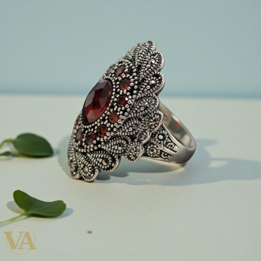 Bague ovale imposante en argent 925, avec une pierre rouge centrale facettée et entourage de marcassites. Design vintage par Vindicta.