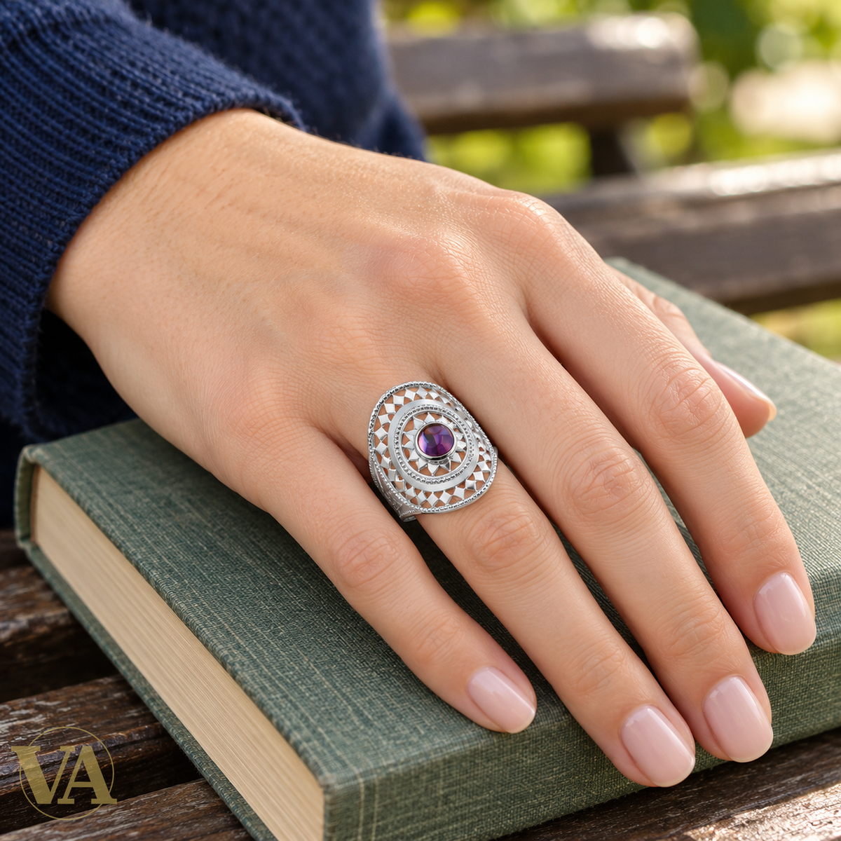 Bague argent 925 motif ajouré et zirconium violet — portée sur une main posée sur un livre
